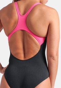 Sort ét stykke badedragt med et pink crossover rygdesign. Glat tekstur med lav rygudskæring og ingen ekstra udsmykninger.