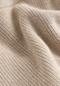 Tissu tricoté beige clair avec une texture côtelée, constitué de fils fins et doux qui créent une surface lisse et continue.