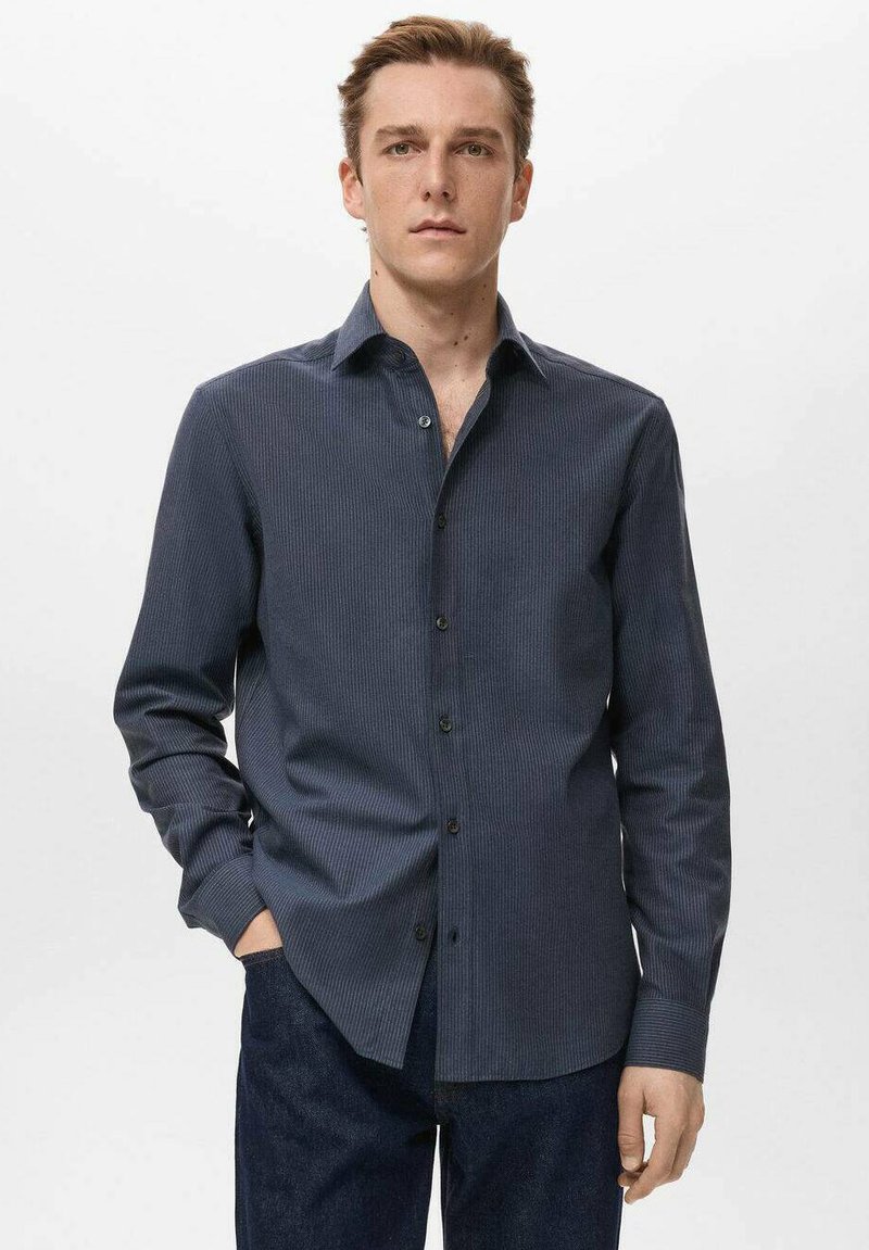 Camisa azul marino de manga larga con sutiles rayas verticales, cuello abotonado y botones negros. Textura suave, corte entallado.