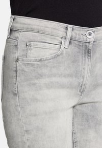 Jasnoszare dżinsy z efektem sprania, z kieszenią z przodu, szlufkami na pasek i metalowym zapięciem.