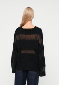 Schwarzer Strickpullover mit lockeren, durchsichtigen gestreiften Einsätzen. Hat einen runden Halsausschnitt und weite, überschnittene Ärmel. Weiche Textur.