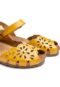 Yellow leather sandals with cut-out floral design, adjustable strap, and cork footbed. Non-slip rubber sole for traction.