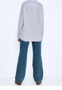 Camicia a maniche lunghe color lavanda chiaro con giromanica sul retro, abbinata a jeans in denim scuro a gamba larga, caratterizzati da un fit morbido e cuciture in vista.
