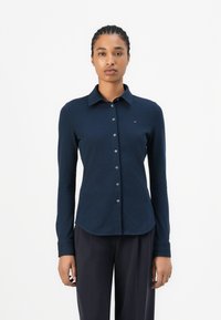 Camicia a maniche lunghe blu navy con colletto, chiusura a bottoni e design aderente. Tessuto morbido e particolare logo discreto sul petto.