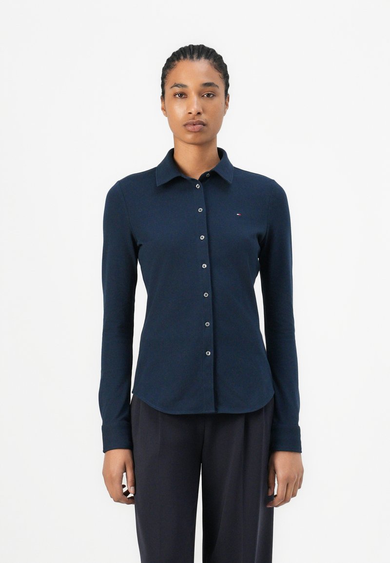 Camicia a maniche lunghe blu navy con colletto, chiusura a bottoni e design aderente. Tessuto morbido e particolare logo discreto sul petto.