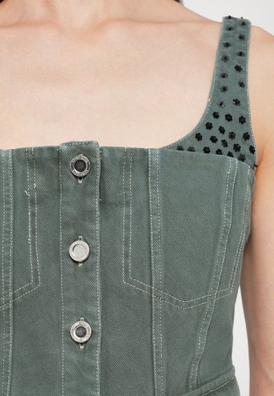 Grünes Denim-Oberteil mit strukturiertem Design, vorne mit Knopfverschluss und einem texturierten, schwarz akzentuierten Schulterriemen mit floralen Mustern.