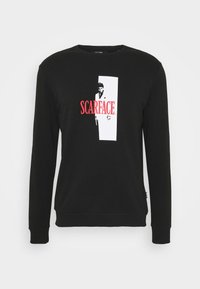 Sudadera negra de manga larga, con un gráfico en rojo intenso que dice "SCARFACE" y un diseño rectangular blanco con la silueta de un personaje.
