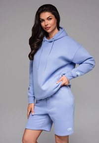 Haut à capuche bleu clair avec cordons de serrage et poche, associé à un short assorti. Tissu doux, coupe décontractée et détails de marque minimaux.