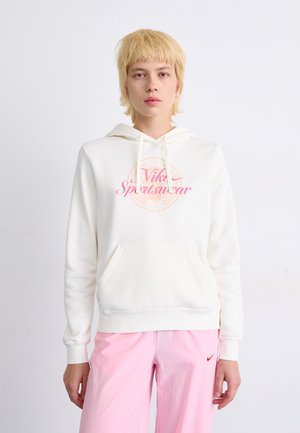 Hvit hettegenser med en framlomme, snøring i hetten og rosa trykk med "Nike Sportswear" på brystet. Kombinert med lyse rosa bukser.