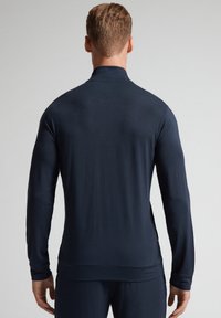 Camiseta de manga larga en color navy con cuello alto, textura suave, diseño ajustado y detalles de costura mínimos, mostrada desde la parte posterior.