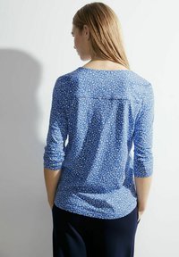 Niebieska wzorzona bluzka z długim rękawem, okrągłym dekoltem i detalami wzdłuż szwów ramion, z geometrycznym wzorem w jaśniejszych odcieniach.