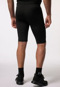 Shorts de sport noirs présentant une coupe ajustée, une texture lisse et une longueur jusqu'au genou. Portés avec des baskets noires et des chaussettes.