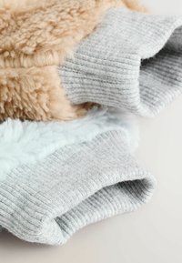 Beżowa, puszysta tkanina i jasnoniebieski pluszowy polar są ułożone warstwowo, wykończone szarymi ściągaczami. Tekstury kontrastują z miękkimi, dotykowymi powierzchniami.