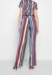 Pantalon rayé multicolore présentant des rayures verticales en rouge, bleu, noir et crème, avec une coupe ample et un détail de poche arrière.