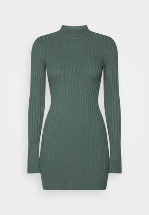 Robe pull côtelée en vert foncé, avec un col montant, des manches longues et une silhouette ajustée. La texture est douce et extensible.