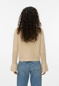 Pull en tricot beige clair, avec un design court et des manches évasées. Porté avec un jean en denim bleu taille haute.