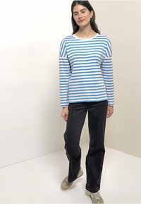 Top a maniche lunghe a righe blu e bianche, con scollo rotondo e vestibilità comoda. Abbinato a pantaloni neri e scarpe chiare.