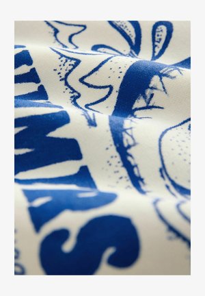 Puuvillakangas kerma-värissä, jossa on rohkea sininen graafinen printti, jossa on abstrakteja muotoja ja tekstiä. Kangas on teksturoitu ja siinä on hienovaraisia yksityiskohtia.