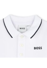Biela polokošeľa s textúrovanou látkou, čiernym lemovaním goliera, tromi bielymi gombíkmi a čiernym logom "BOSS" na ľavej strane hrudníka.