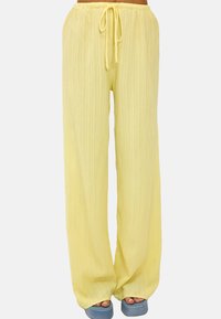 Pantalones anchos de color amarillo claro con una tela texturizada, que cuentan con una cintura ajustable y un corte holgado, combinados con sandalias de plataforma azules.