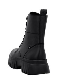 Bottine en cuir noir avec une semelle épaisse, un talon surélevé, un bout rond et un design à lacets. Dotée d'une languette pour un enfilage facile à l'arrière.