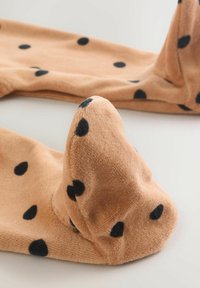 Beige Fleece-Stoff mit schwarzen Tupfen, der an einem Ende ein einzigartiges spitzes Design aufweist, das ein weiches, strukturiertes Erscheinungsbild erzeugt.