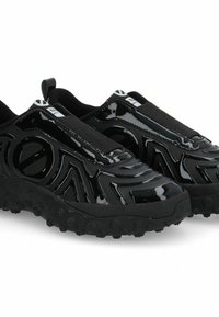 Scarpe nere slip-on realizzate in materiale lucido con motivi testurizzati, cinturini elasticizzati e una suola in gomma robusta con piccole sporgenze.