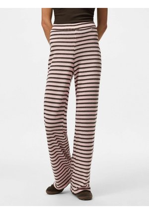 Personne portant un pantalon large rose et noir à rayures zigzag horizontales, associé à un haut noir et des chaussures noires.