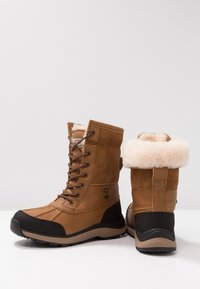Bottes imperméables marron en suède et matériaux synthétiques avec un revers en fausse fourrure, fermeture à lacets et semelle en caoutchouc noire.