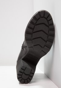 Suela de bota negra con ranuras y estrías profundas para tracción, hecha de goma, con una base rígida y plana y un ligero tacón.