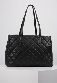 Bolsa de tote de cuero negro con acolchado, forma rectangular, doble asa para el hombro y textura de patrón de diamantes en el exterior.