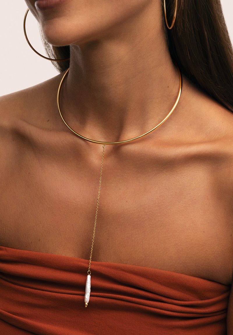 Goldene Choker-Halskette mit einem glatten, kreisförmigen Design und einem Anhänger aus einer weißen, länglichen Perle, die an einer zarten goldenen Kette hängt.