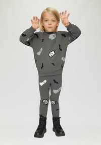 Grauer Pullover und Leggings mit Geister- und Fledermaus-Mustern. Weicher Stoff, lockere Passform und kombiniert mit schwarzen Combat-Stiefeln.