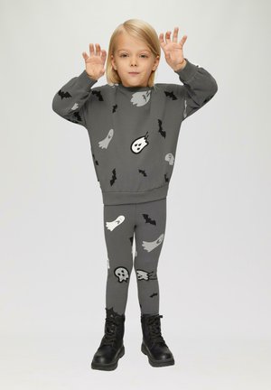Szary sweatshirt i legginsy z wzorami duchów i nietoperzy. Miękka tkanina, luźny krój, zestawione z czarnymi butami wojskowymi.