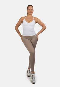 Biała bluzka na ramiączkach w zestawieniu z jasnobeżowymi legginsami. Ubranie charakteryzuje się gładką fakturą i logo na nogawce legginsów. Całość dopełniają białe sneakersy.