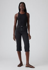 Svart ribbet tanktopp kombinert med høyhælte svarte denim cubusbukser, med en tettsittende silhuett og minimale hardware-detaljer.