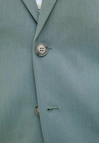 Blazer verde deschis din țesătură texturată, cu închidere prin nasturi și accente subtile de cusătură. Design clasic de rever și croială ajustată.