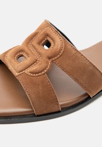 Sandale en daim marron avec deux larges brides, chacune présentant une découpe et un rembourrage, sur une semelle intérieure beige avec une semelle noire.