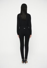 Set de top și pantaloni negri tricotate, cu design ajustat, material texturat și accente nervurate. Asortat cu pantofi negri cu toc înalt.