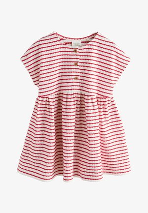 Fată zâmbitoare în rochie cu dungi roșii culege o portocală de pe un copac citric luxuriant într-o grădină însorită în aer liber.