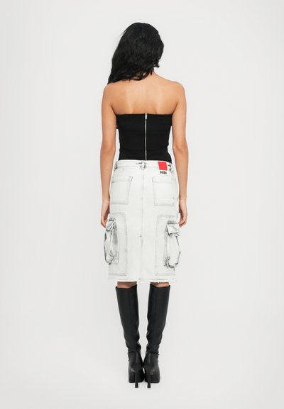 Haut noir sans bretelles avec une fermeture éclair dans le dos, associé à une jupe midi en denim blanche avec des poches cargo et une étiquette de marque rouge. Bottes noires jusqu'au genou.