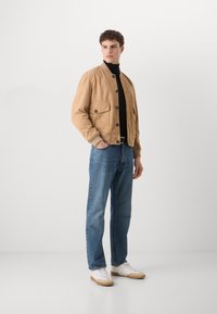 Tamnasti suede bomber jakna s rebrastim manžetama, crna rolka, plave traperice i bijele tenisice s bež akcentima.