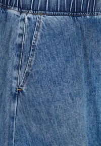 Denim tkanina svijetlo plave boje s blago izblijedjelim uzorkom, s elastičnom gumom u struku i bočnom džepom s vidljivim žutim šavom.