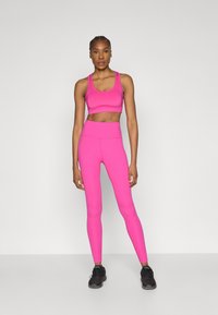 Set de sutien sport și colanți în roz aprins, confecționat dintr-un material elastic, având un design mulat și talie înaltă pentru susținere și confort.