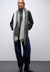 Gray and white striped scarf layered over a gray sweater, paired with dark blue wide-leg jeans and black ankle boots. Plain background.
