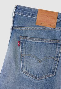Jasnoniebieskie dżinsy z denimu z naszywką ze skóry z napisem Levi Strauss & Co. Kieszeń ozdobiona charakterystycznym wzorem szwów oraz czerwoną metką.