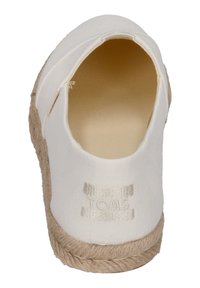 Bílé espadrilky s plátěným svrškem a tkanou jutu podrážkou. Mají hladkou, zaoblenou špičku a viditelné logo "TOMS" na boku.
