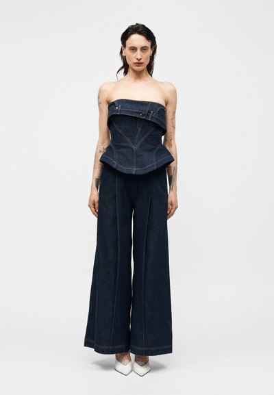 Μοντέλο που φοράει σκοτεινό denim κορσέ τοπ χωρίς τιράντες με φαρδιά μέση και αντίστοιχο παντελόνι φαρδιάς γραμμής, σε συνδυασμό με λευκές μυτερές γόβες.