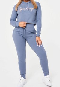 Světle modrá cropped mikina s kapucí a logem "Gym King", doplněná o odpovídající tepláky. Měkká látka, dlouhé rukávy a nastavitelný pás na šňůrku.