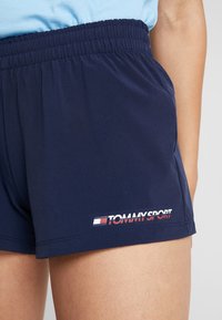Tummansinisiä urheilushortseja, jotka on valmistettu kevyestä kankaasta, elastisella vyötäröllä ja Tommy Sport -logolla valkoisena, punaisena ja sinisenä helmaosassa.